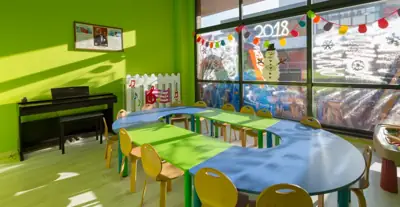Piyano ve oval çalışma masası bulunan güneşli anaokulu sınıfı