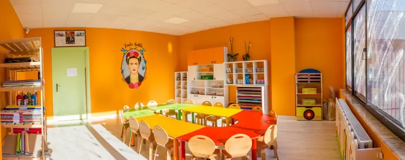 Sanat sınıfında sarı ve kırmızı çocuk masaları, ahşap sandalyeler ve raflar
