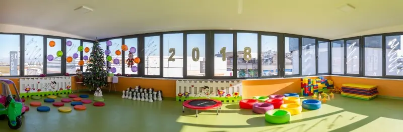 Geniş pencereli oyun salonunda minderler, mini trambolin ve oyuncaklar