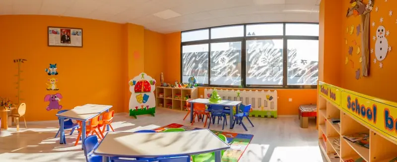 Turuncu duvarlı sınıfta alçak masalar, oyuncak rafları ve oyun köşesi